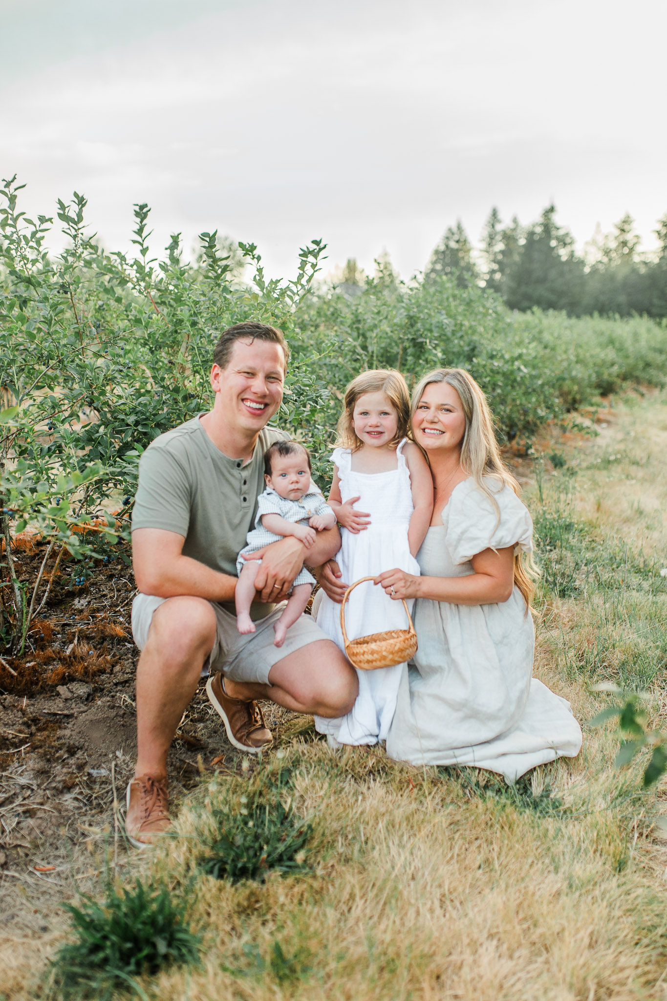 A family of four smiling at the camera snuggled together at a blueberry field