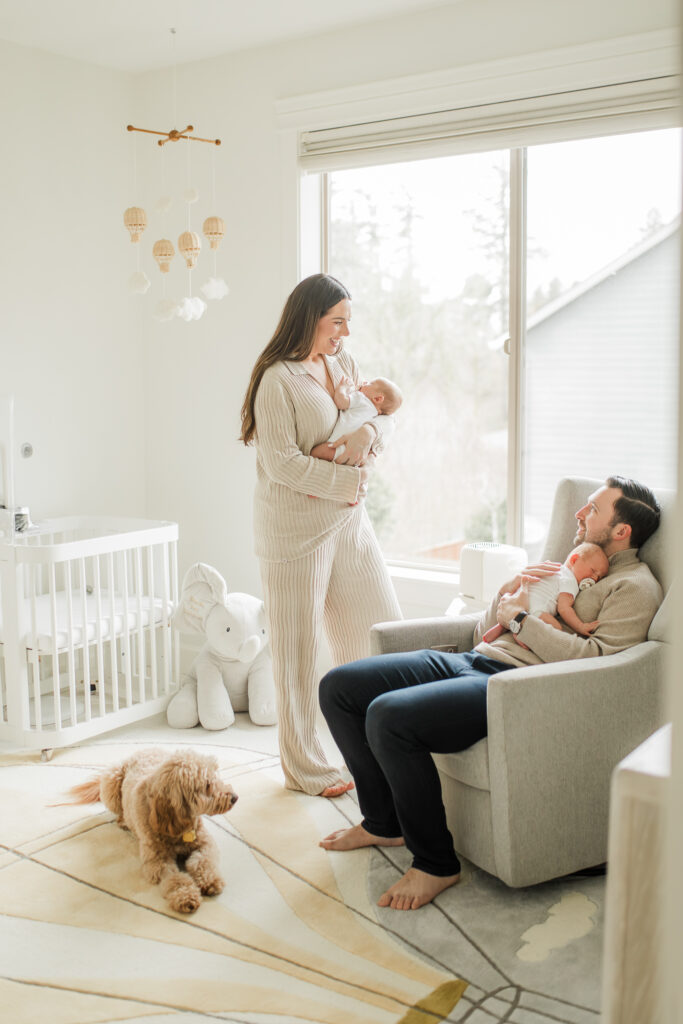 Twin newborn photo session in home with both parents in a beautifully decorated nursery and dog lying on the floor.