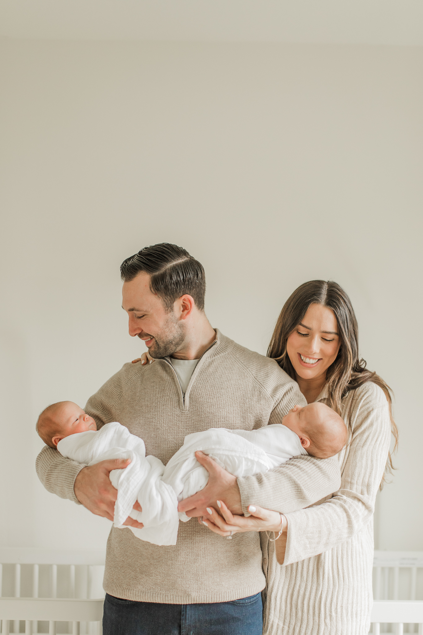 parents lovingly holding and looking at their twin newborn babies while they are in their neutral nursery