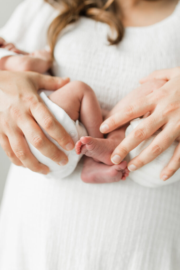 Mother holding her newborn twin babies snuggled close with a close up on the babies' toes.