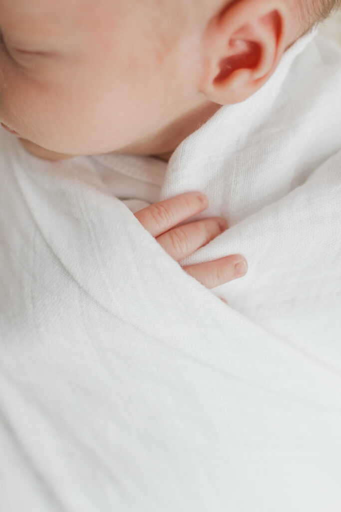 close up of a newborn baby fingers and ear details while they are swaddled in a white swaddle