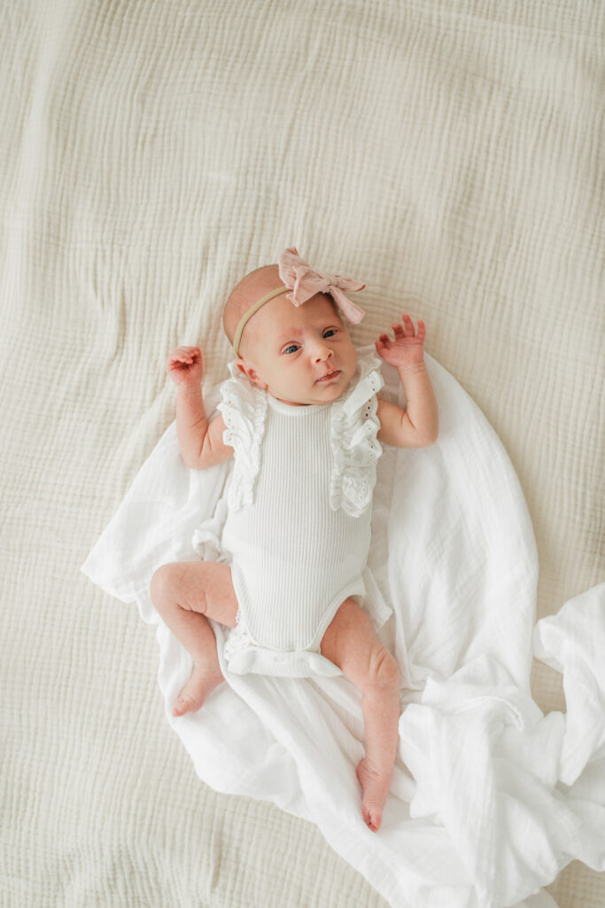 Twin newborn photo session in studio with a newborn baby girl lying on cozy blankets and swaddles.