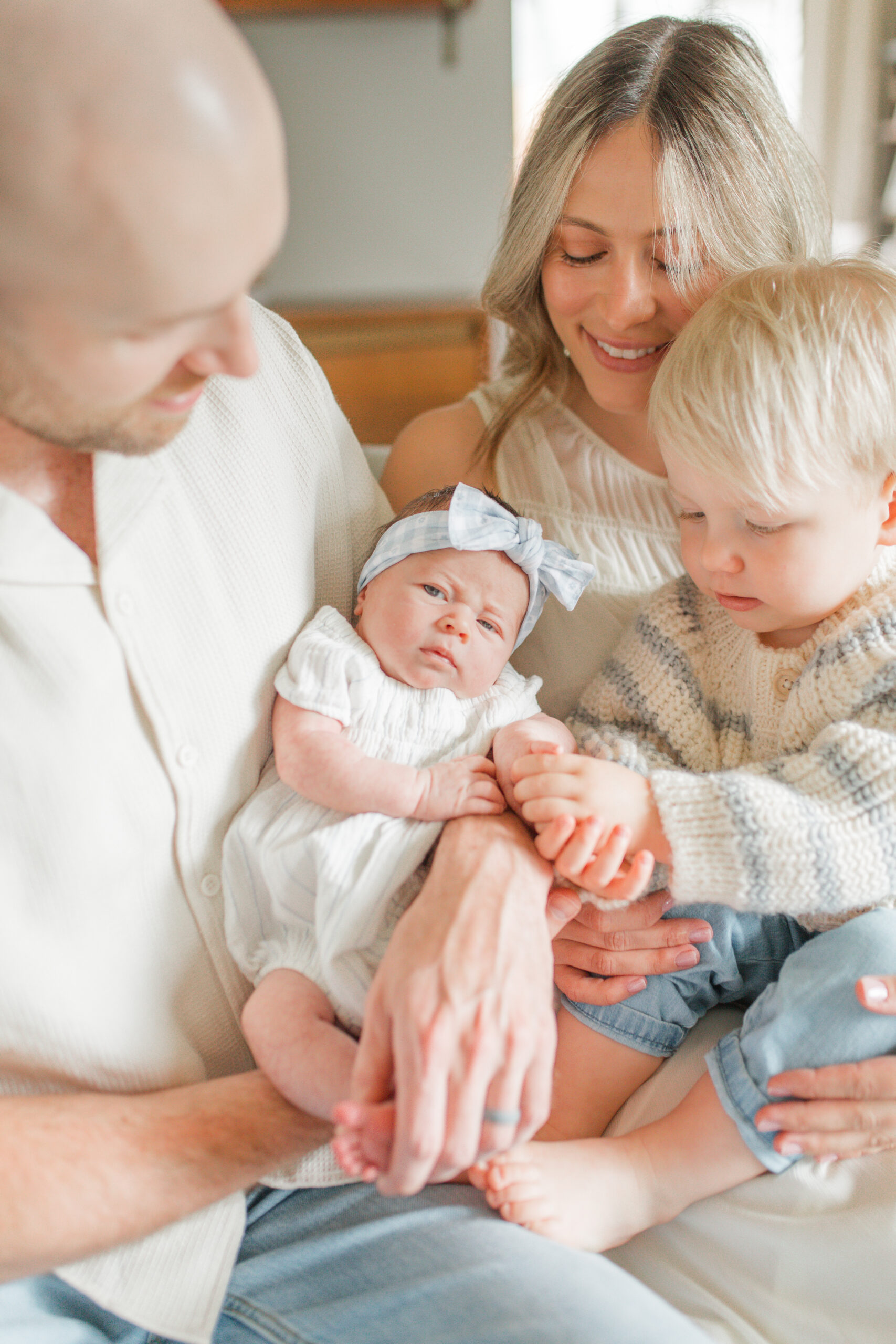 family snuggled on the couch holding their newborn baby girl and toddler son during their newborn photo session