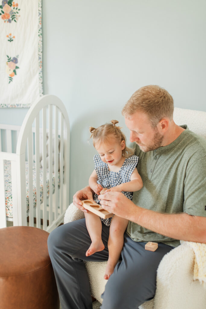 a father holds her toddler daughter and they play with toys together