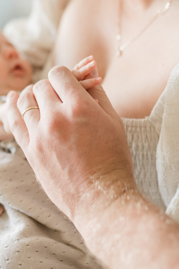 a close up detail photo of a parent holding their newborn baby's hand. you can see the size difference of the newborn's fingers compared to the dad's hand.