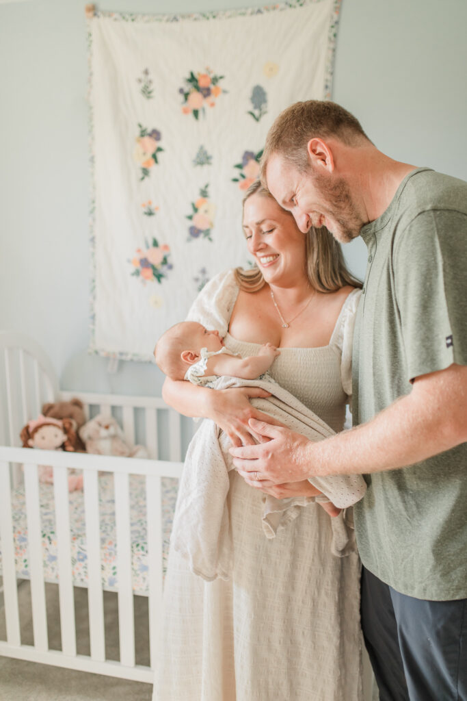 parents hold their newborn baby and look down at her smiling