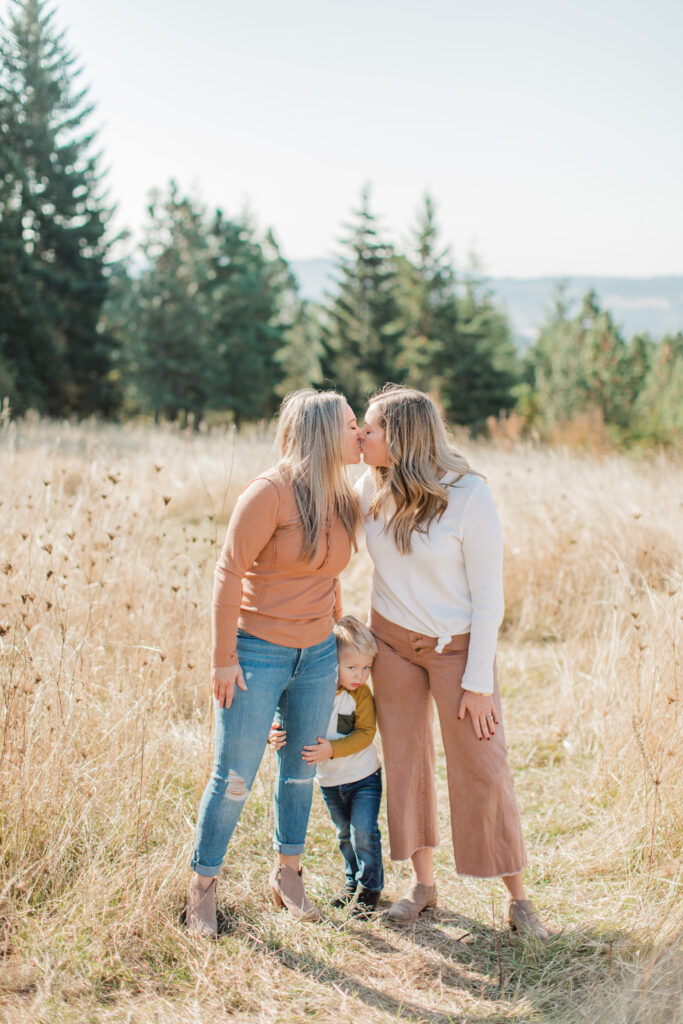 two moms kiss with their toddler son in the middle hugging them both