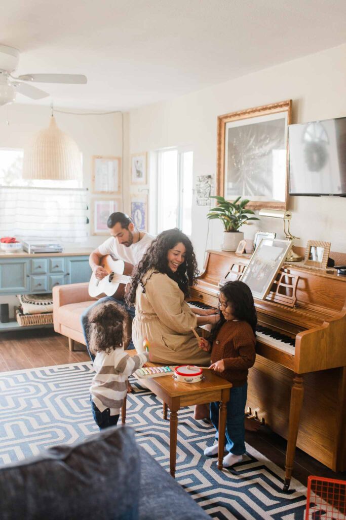 Lifestyle in-home family photo of parents and children playing piano and guitar together in a bright Vancouver WA living room.