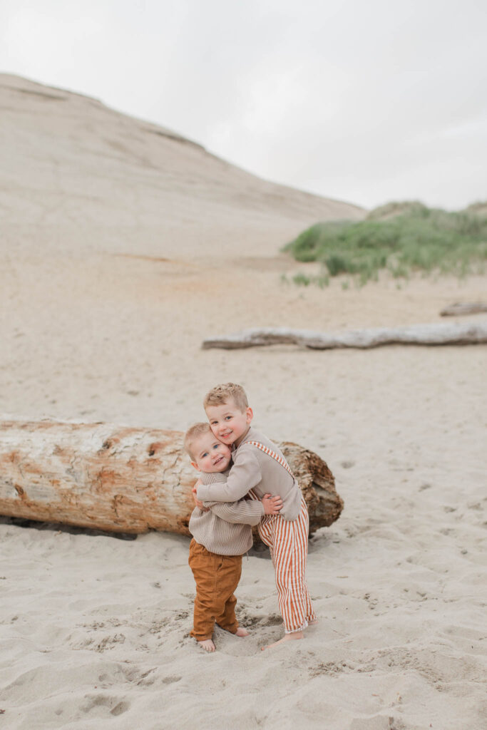 Two boys playing in sand during lifestyle Oregon coast maternity session