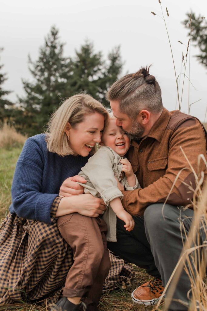 Joyful family of three laughing together in a scenic fall landscape, capturing candid outdoor family moments in Camas WA.