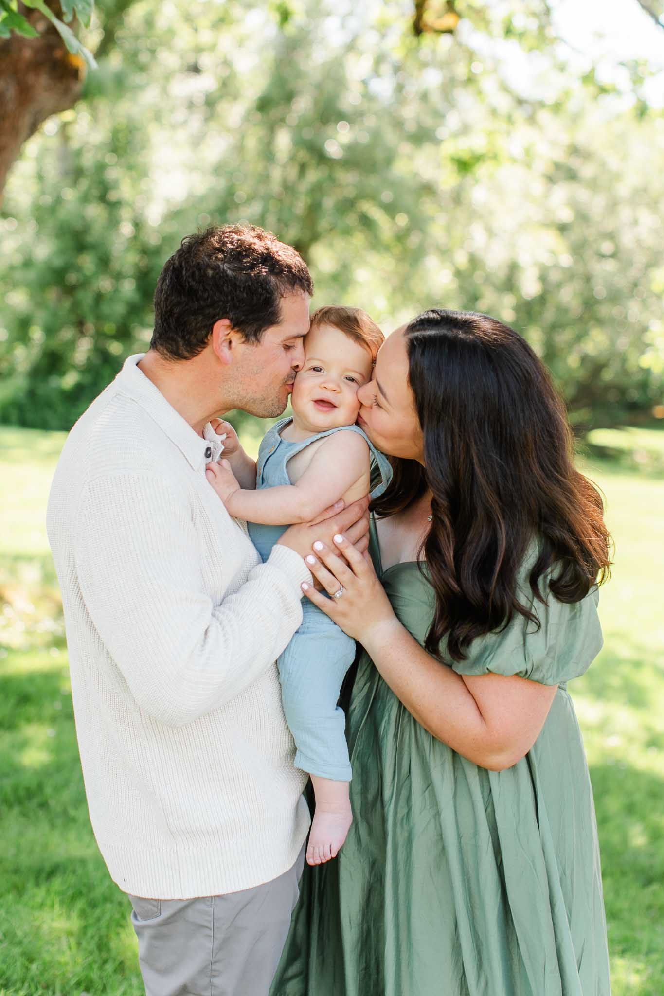 Family kissing their one year old baby in a dreamy golden light Camas, WA park.