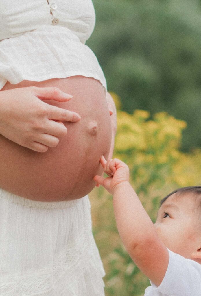 Toddler pointing to mother's pregnant belly during outdoor maternity photos