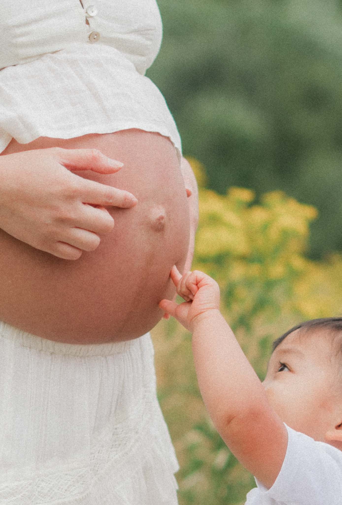 Toddler pointing to mother's pregnant belly during outdoor maternity photos